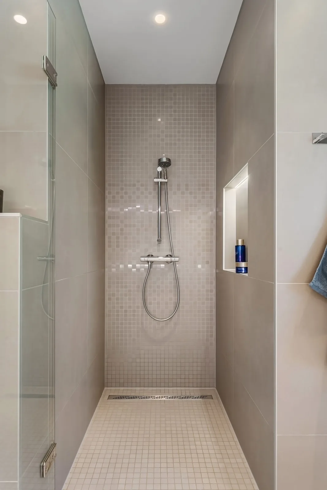 Neutral tiled walk-in shower with chrome mixer and hand shower