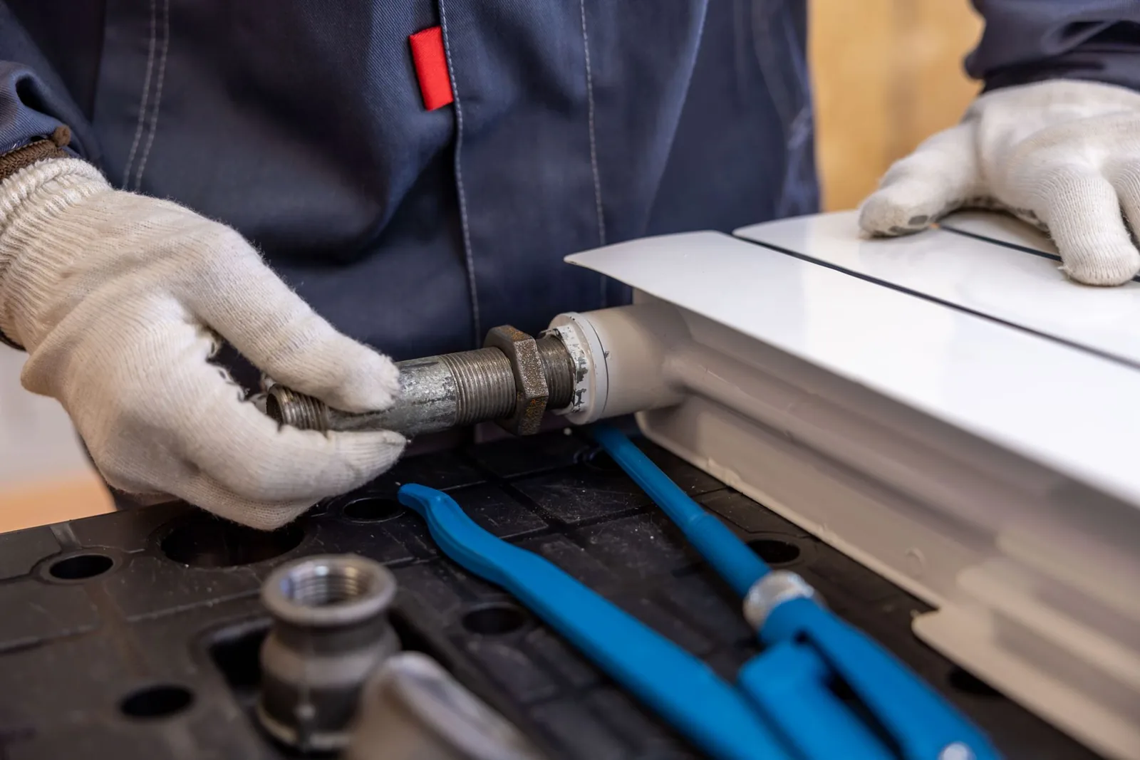 Gloved hands fitting a connection to a panel radiator on a workbench